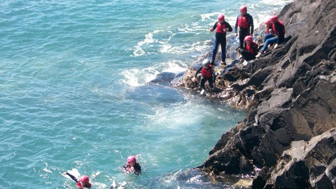 Group of people coasteering in Pembrokeshire enjoy swimming by the sea