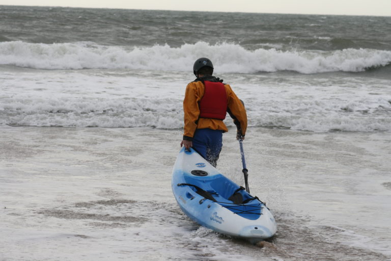 A person holding a sit-on-top kayak getting started for surf kayaking.
