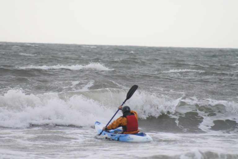 A person doing kayak surfing, braving the waves of the ocean.