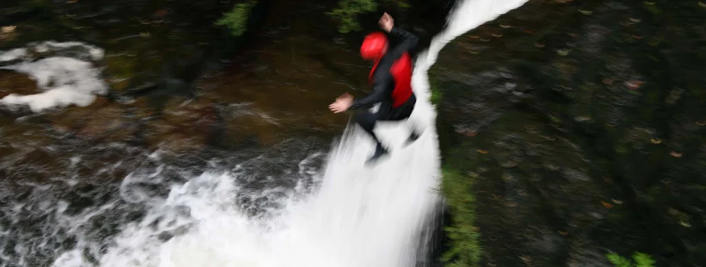 person jumping near a waterfall