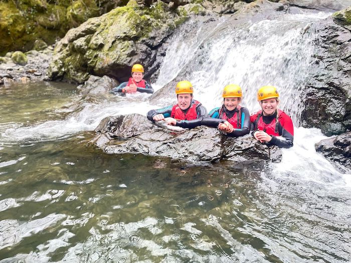 gorge walking group in water next to a waterfall land rock 