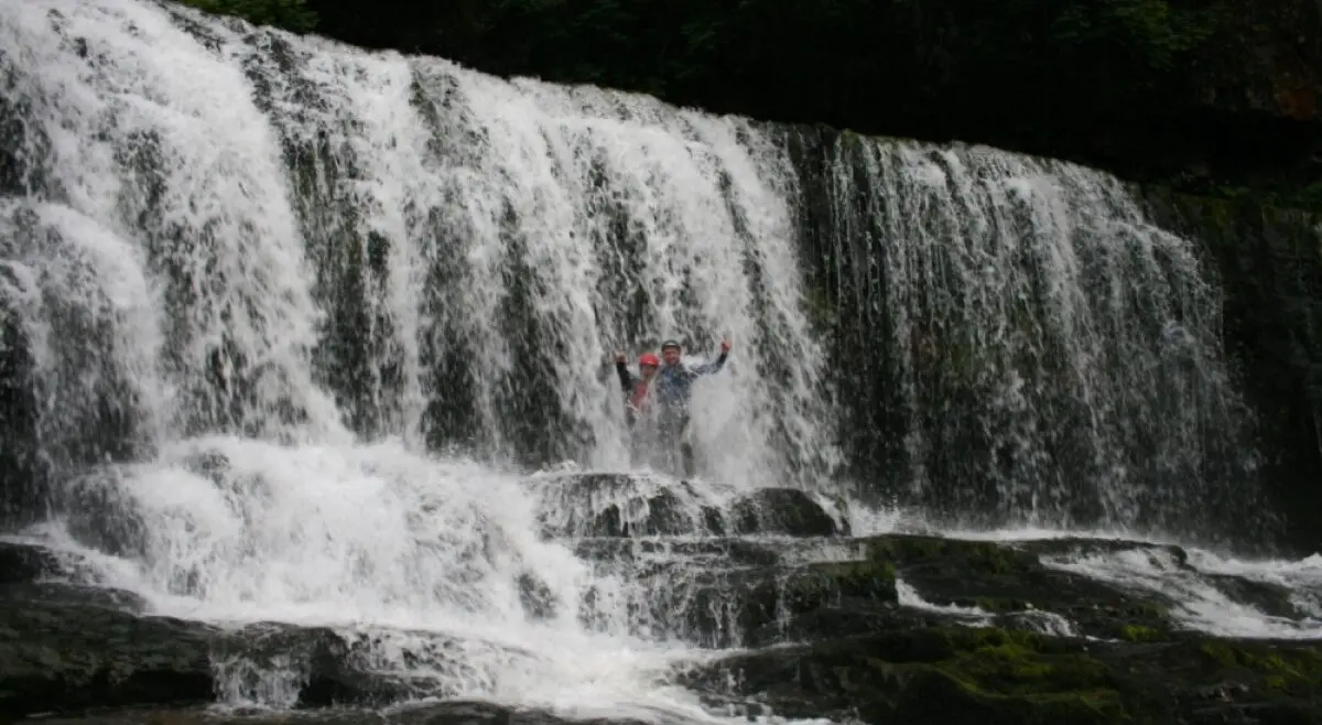 Two persons in the middle of a wide waterfall during their Canyoning in Wales activity.