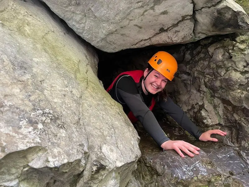 A woman gorge scrambling in Wales, smiling for a picture inside a small cave entrance