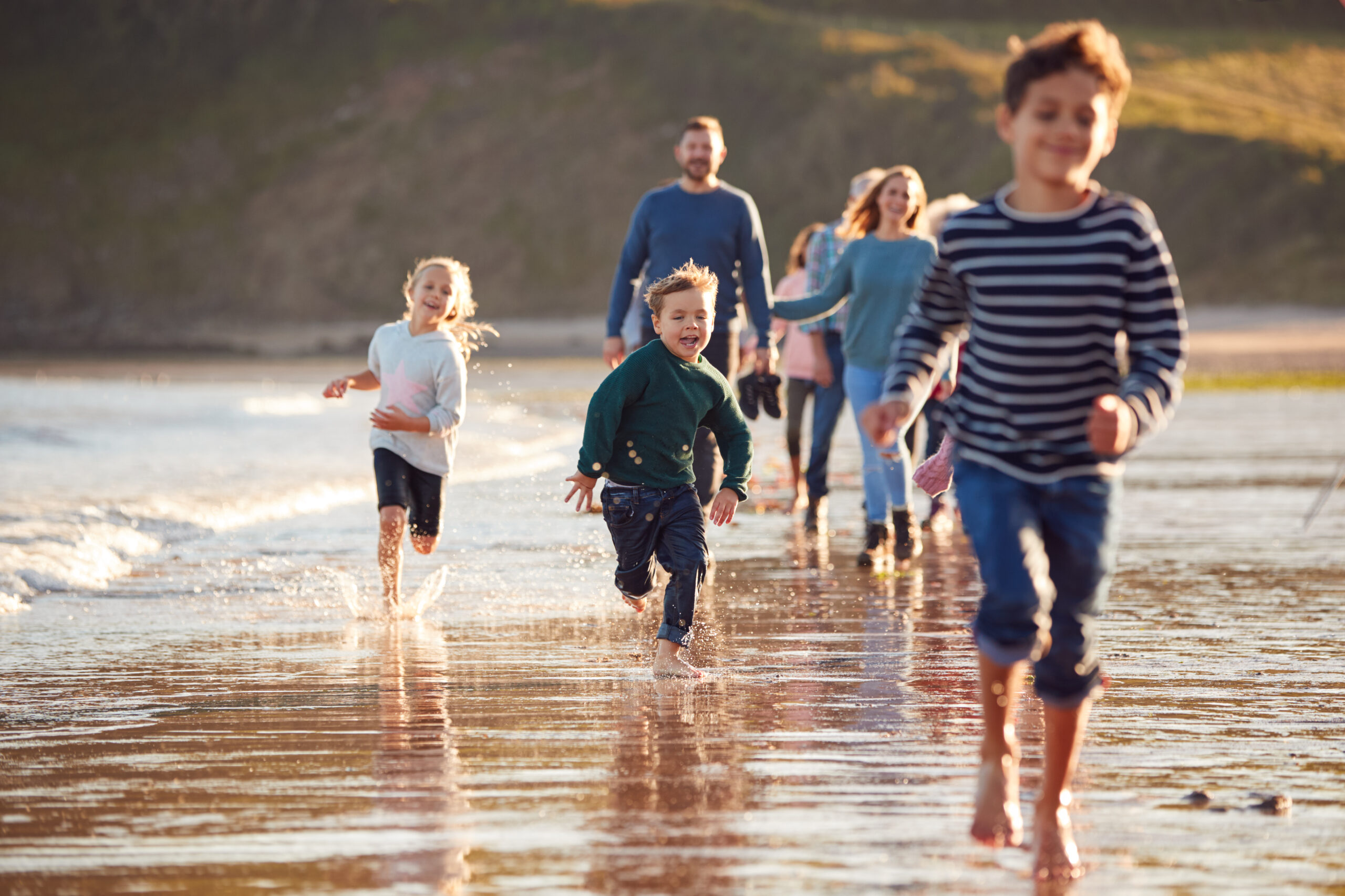 Three kids running along the beach in South Wales with their parents at the back