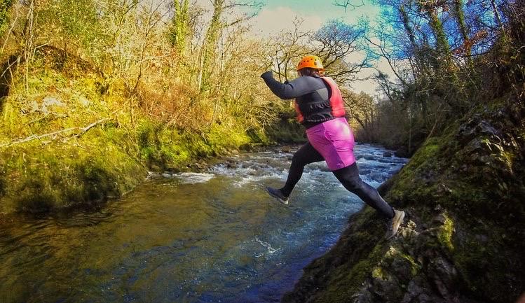 A woman jumping off a cliff during a canyoning adventure in Cardiff