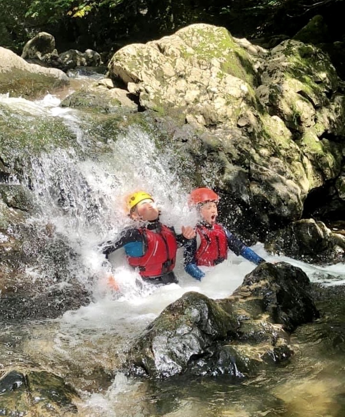 Two kids enjoy soaking in the waterfall during family gorge walking adventure