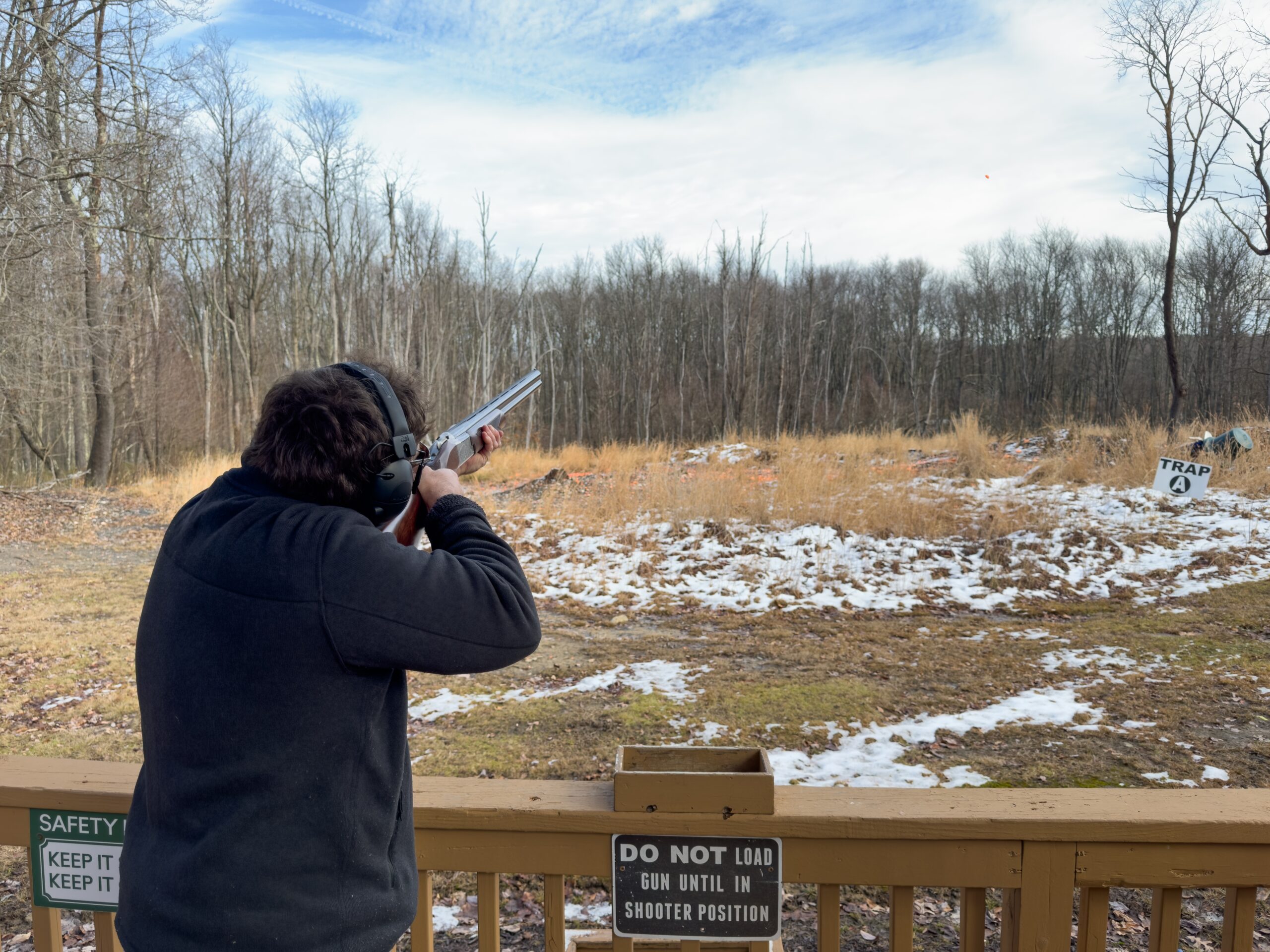 A man holding a gun, aiming for his target at a clay pigeon shooting ground