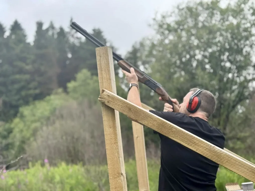 A man holding a shotgun aiming for his target during his clay pigeon shooting adventure in Wales