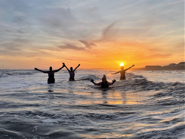 Four individuals enjoy dipping in the sea during sunset