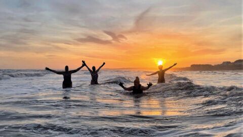 Four individuals enjoy dipping in the sea during sunset