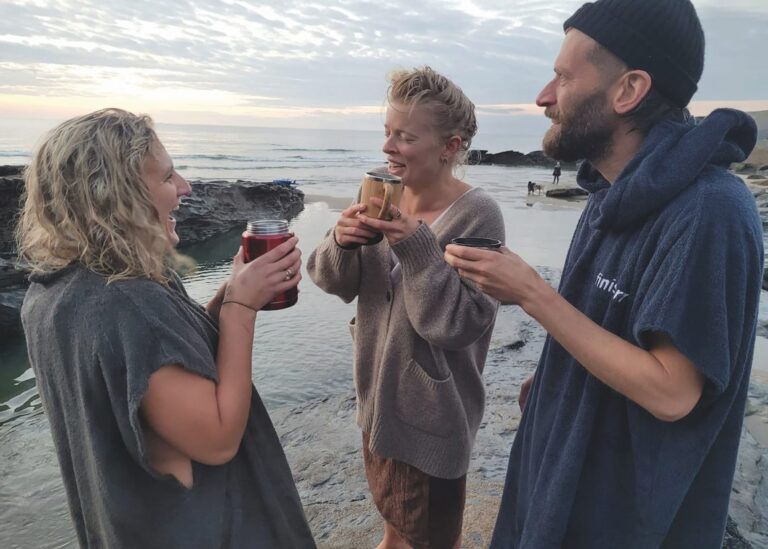 Three people each holding a cup while chatting by the beach