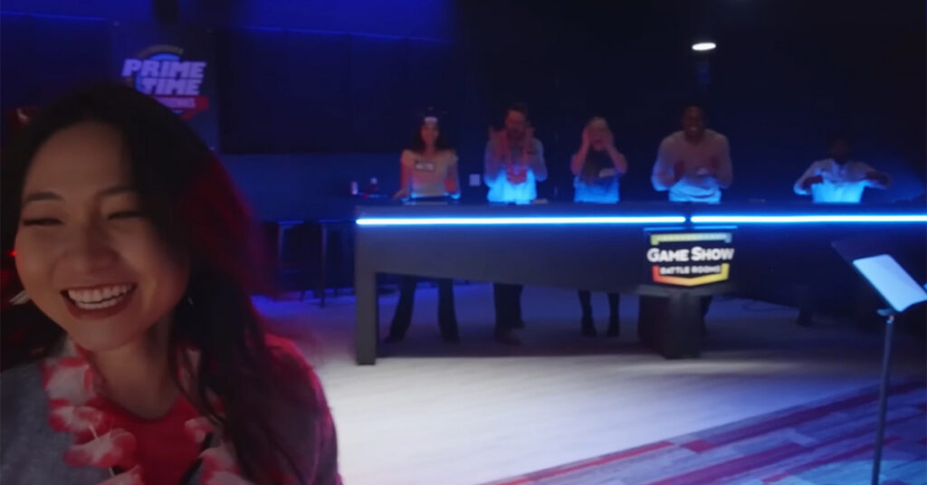 A smiling woman at a game show with a team of participants at the background