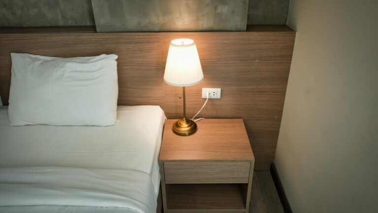 Elegant bedroom setup with a lamp on a wooden nightstand, creating a cozy ambiance.