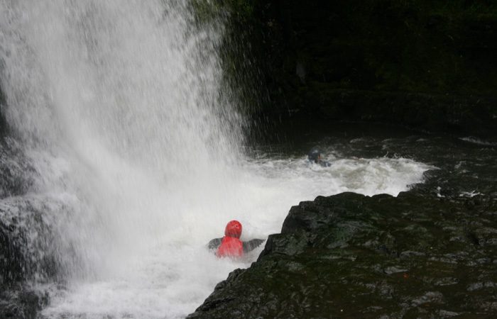 person swimming near waterfall