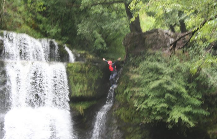 person jumping into water near a waterfall