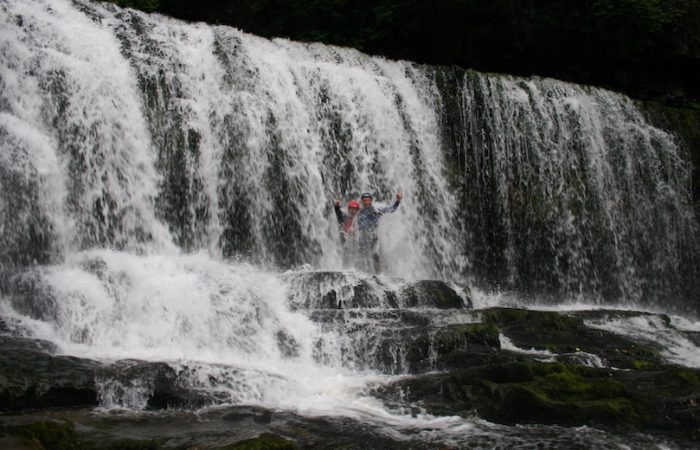 people gorge walking under a waterfall